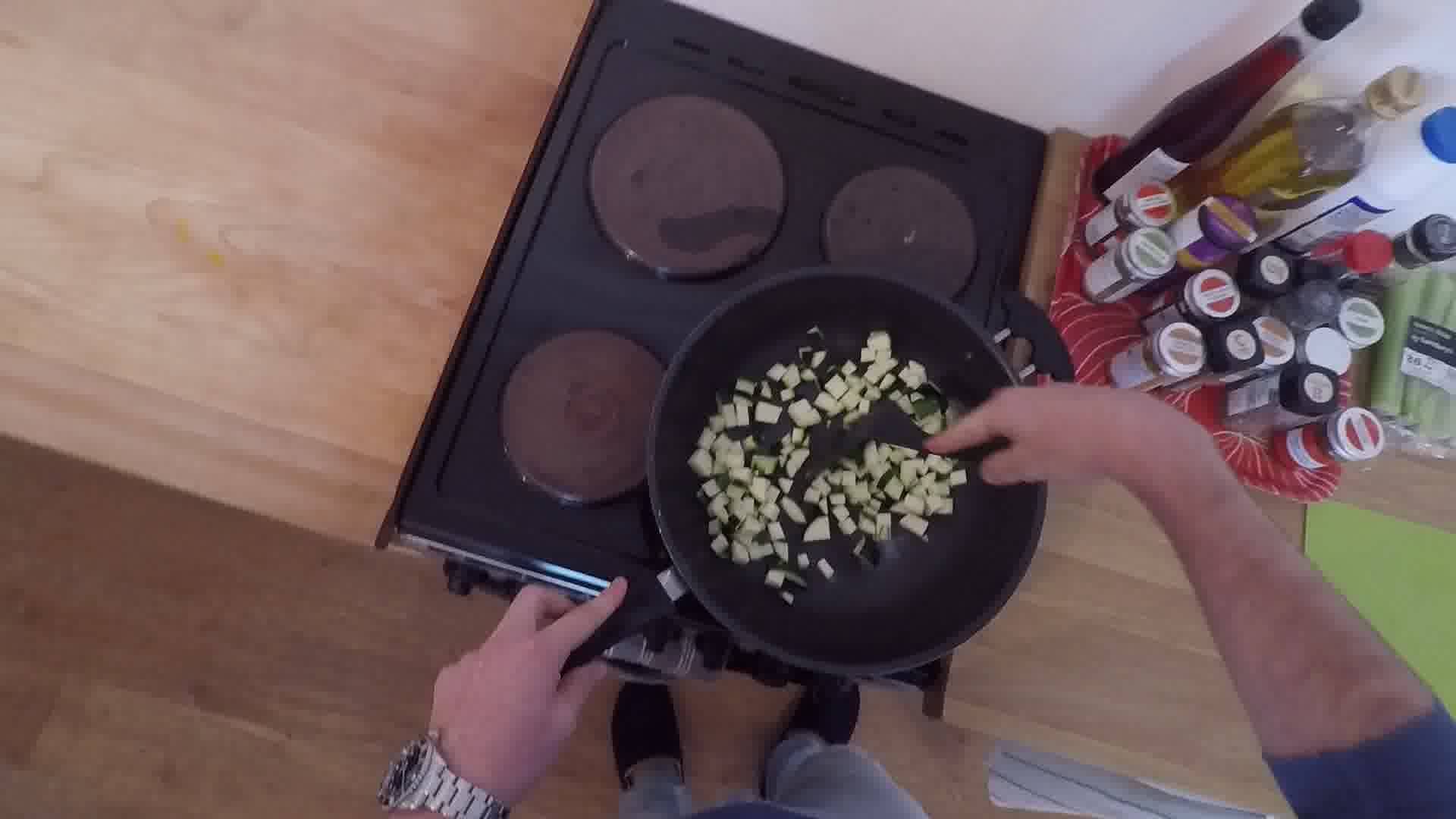 Egocentric frame: a hand lifting a pan over a hob in a real kitchen
